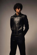 Person wearing a black leather jacket and pants against a gray background
