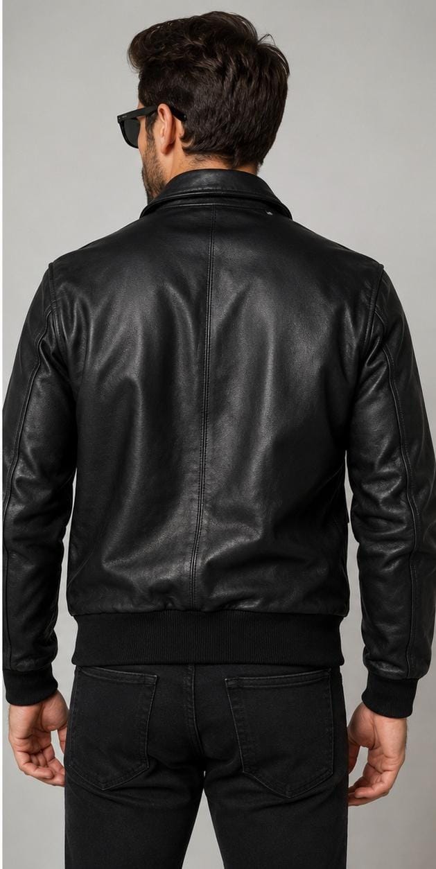 A man viewed from behind wearing a black leather jacket and black pants against a plain gray studio background.