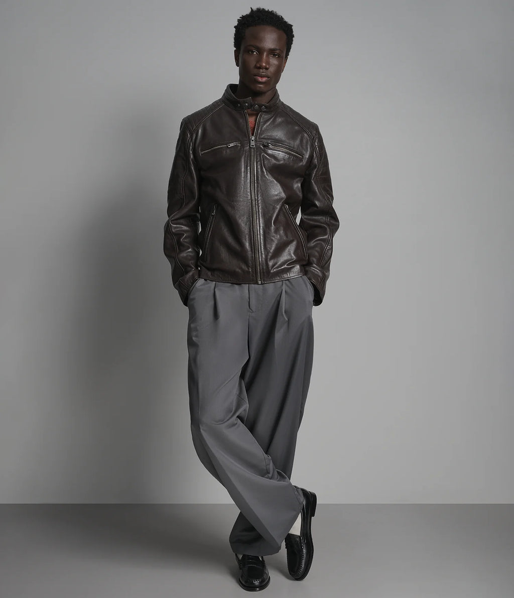 Man wearing a dark leather jacket and gray pants against a plain background