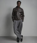 Man wearing a dark leather jacket and gray pants against a plain background