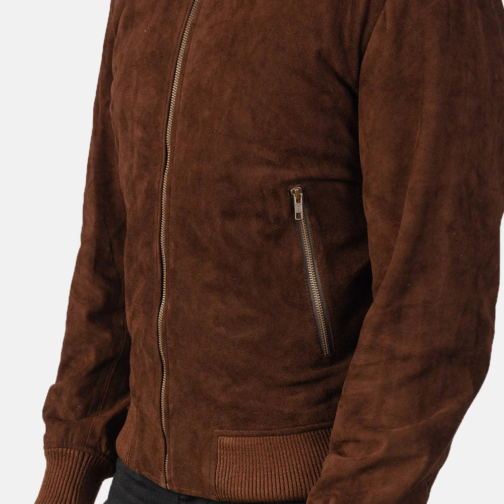 A close-up of a brown suede or faux-suede jacket with a front zipper, a vertical zippered chest pocket, and ribbed cuffs and hem, shown on a model against a light gray background.