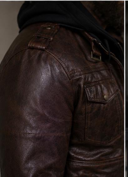 Close-up of a dark brown distressed leather jacket with a black hood, showing the shoulder, side pocket, and belt buckle details.