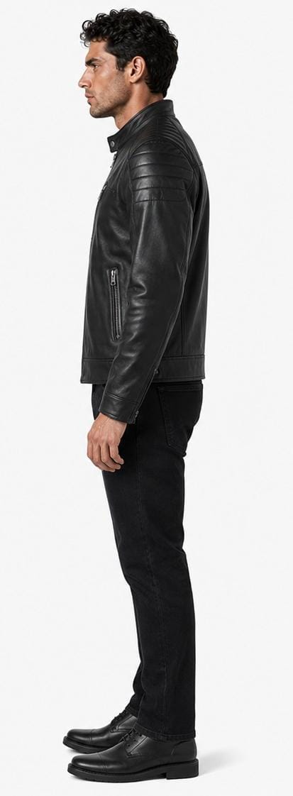 A man shown in profile wearing a black leather jacket, black pants, and black shoes against a plain light gray studio background.